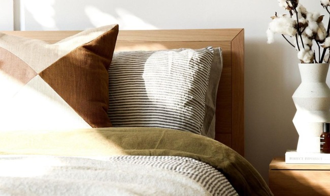 swath of sunlight shines across a well made bed and bedside table with a vase of cotton plants